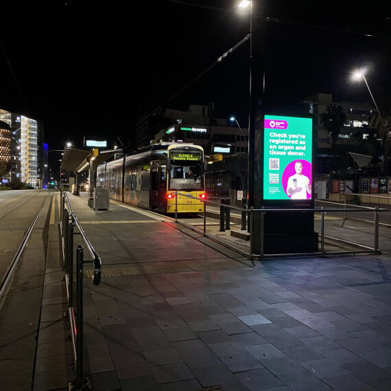 A brightly lit LED advertising panel at a tram stop in Adelaide.