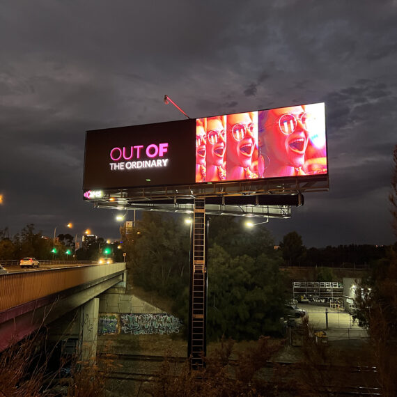 A brightly lit LED billboard sign over a bridge.